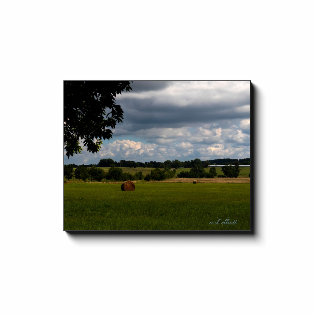 Gallery-wrapped canvas print featuring a rural Arkansas hayfield with round bales beneath a dramatic cloudy sky.