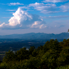 View from the Blue Ridge Parkway near Roanoke, Virginia, showing distant farms, layered blue mountains, green forest, and large white summer clouds.