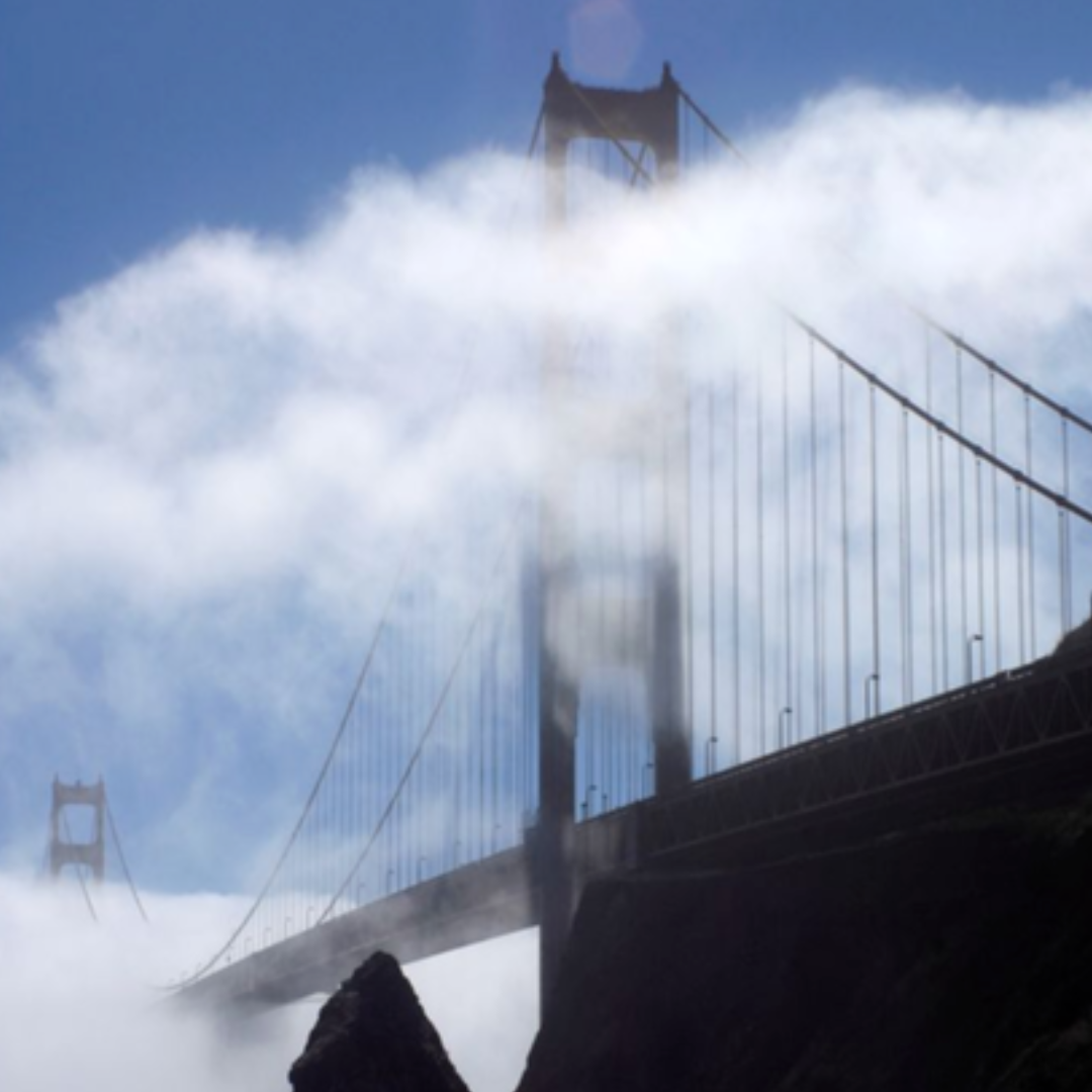 Golden Gate Bridge rising through thick coastal fog beneath a blue sky in San Francisco, California.
