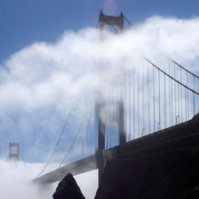 Golden Gate Bridge rising through thick coastal fog beneath a blue sky in San Francisco, California.