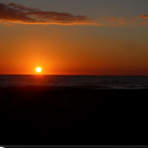 Close-up view of a brilliant orange sunrise rising above the Atlantic Ocean at Virginia Beach, Virginia, with warm morning light illuminating the horizon.