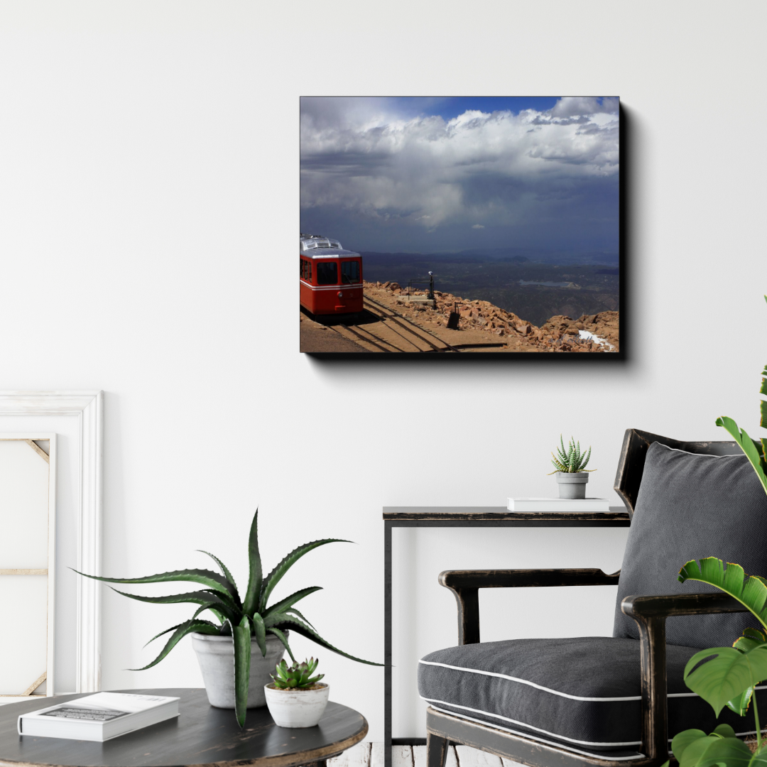 Pikes Peak Cog Train canvas photograph displayed above a dark armchair in a modern room with potted plants and neutral decor.
