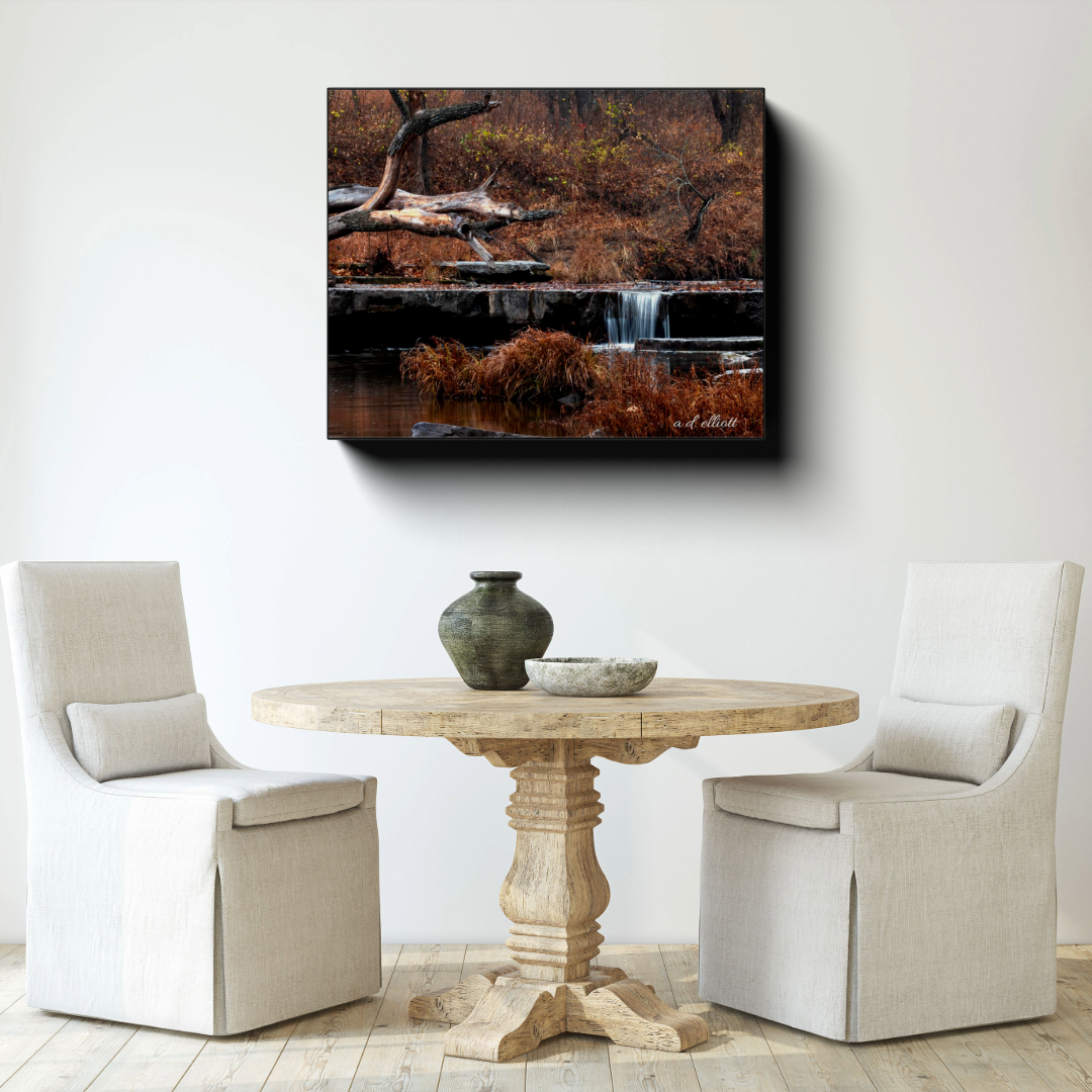 Sand Creek Upper Cascade canvas photograph displayed above a round wooden dining table between two upholstered chairs in a bright room.
