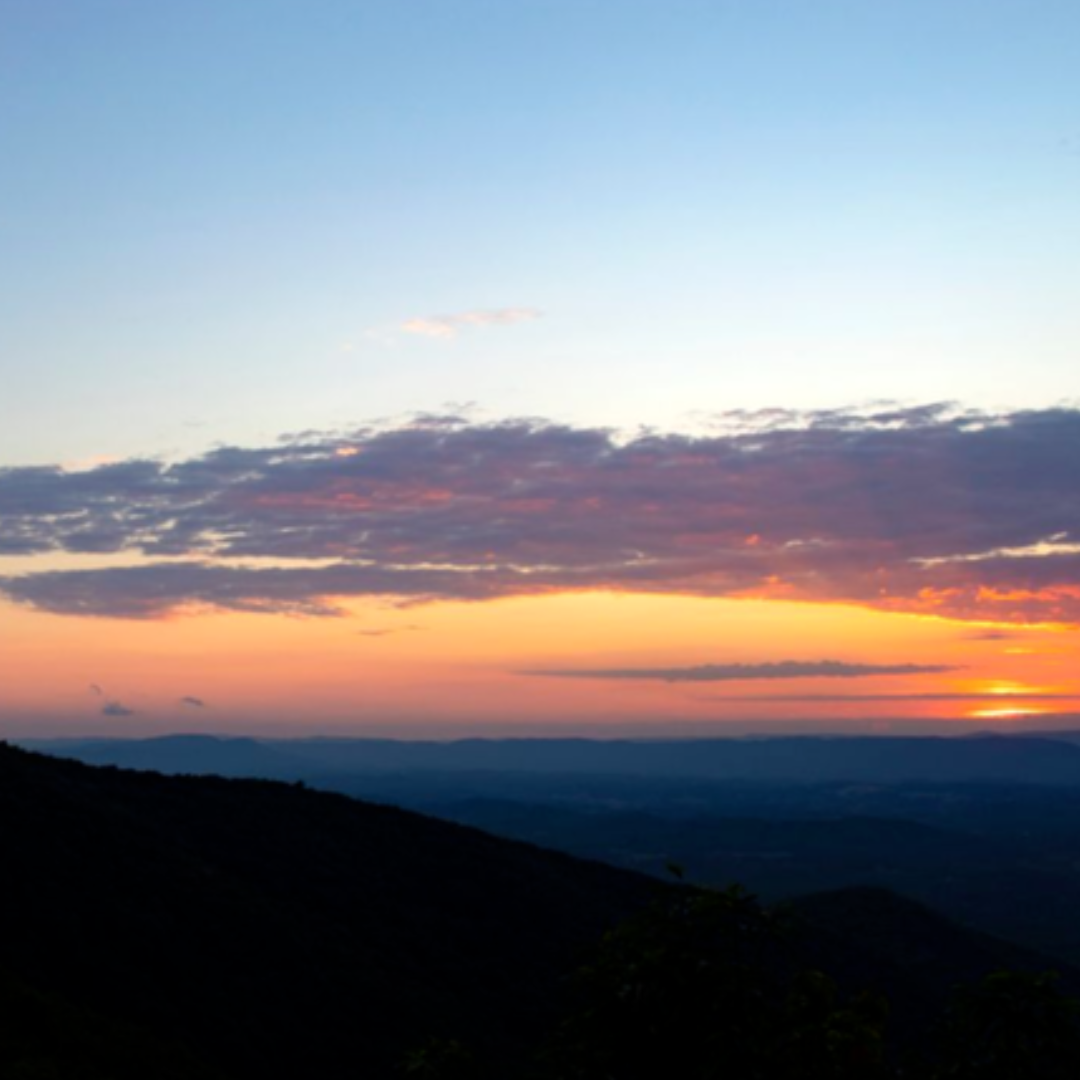 Sunset over layered mountain ridges near Roanoke, Virginia, with a glowing orange horizon beneath a band of clouds along the Blue Ridge Parkway.