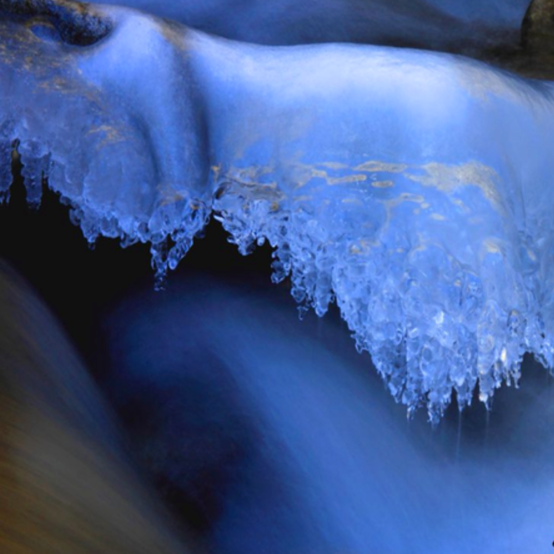 Close-up photograph of flowing water passing beneath a shelf of ice in Golden, Colorado.