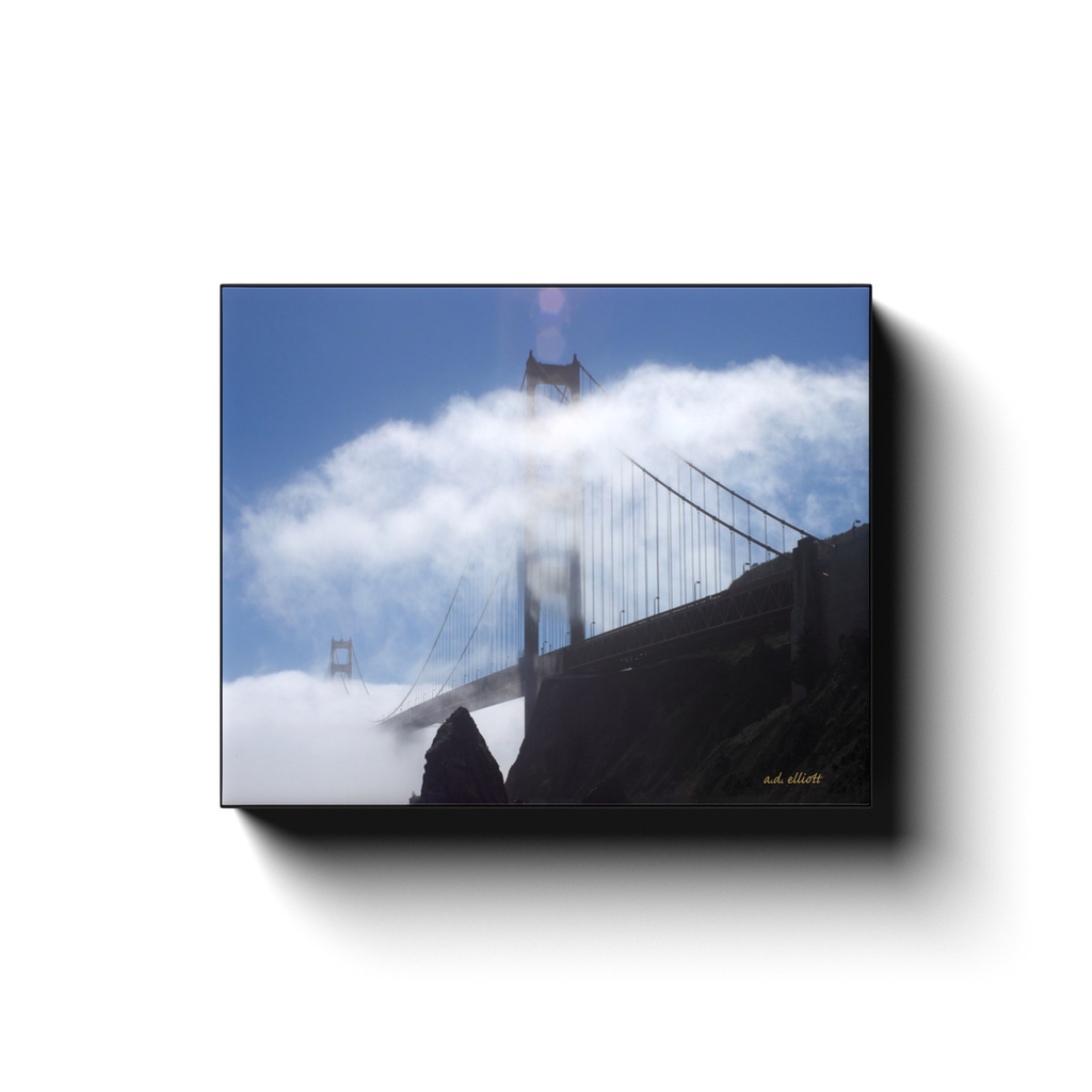A photograph of San Francisco's Golden Gate Bridge behind clouds. Taken by the Arkansas photographer a.d. elliott #TaketheBackRoads  Printed on high quality, artist-grade stock and folded around a lightweight frame to give them a gorgeous, gallery-ready appearance. With acid-free ink that will last without fading or chipping, Features a scratch-resistant UV coating. Wipes clean easily with a damp cloth or to remove dust, vacuum gently using a soft brush attachment.